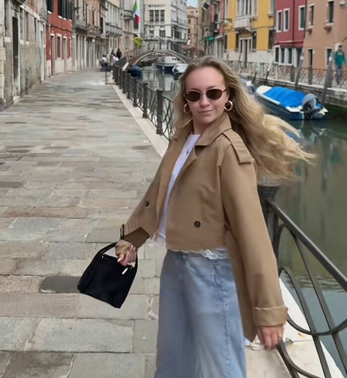 An influencer with long blonde hair, sunglasses, and a trench coat walking alongside a Venetian canal, posing for a photo. An influencer with long blonde hair, sunglasses, and a trench coat walking alongside a Venetian canal, posing for a photo.