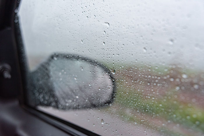 A car window covered in rain, viewed from inside, with a blurred side mirror. Reflects conflict and control in marriage. A car window covered in rain, viewed from inside, with a blurred side mirror. Reflects conflict and control in marriage.