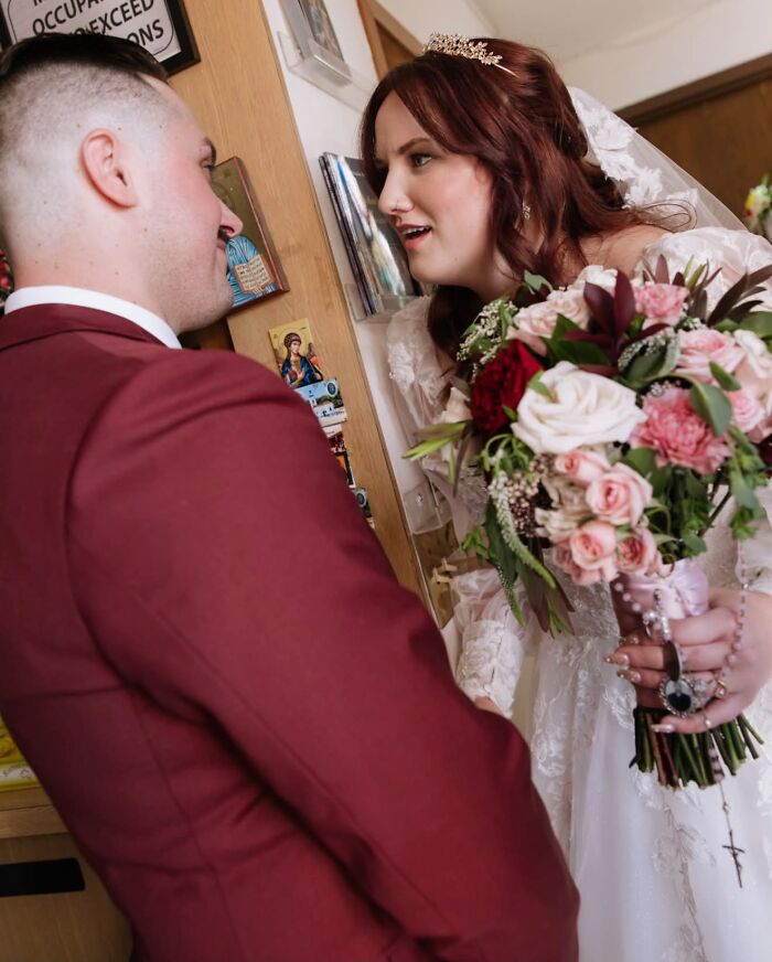 A bride in a white dress and veil with a bouquet looks up at her groom in a funny wedding photo.