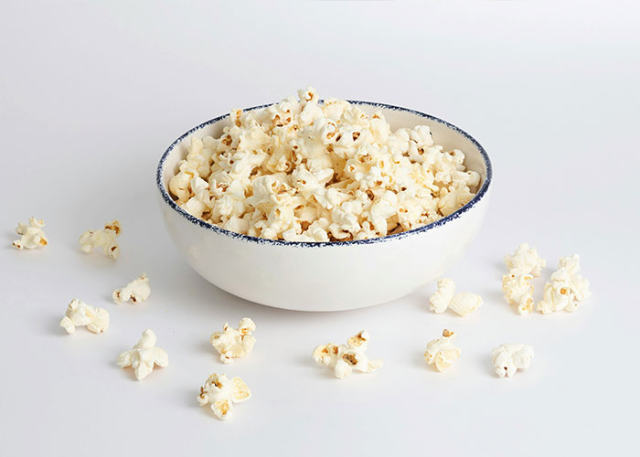 A bowl of popcorn on a white surface, representing foods parents should never allow their children to consume.