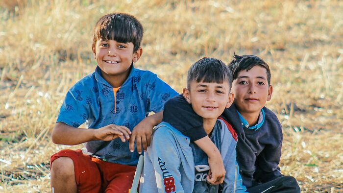 Three young boys smiling and sitting closely together in a sunny, dry field, for stories about controlling what a boyfriend eats.