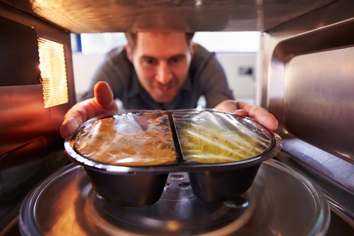 A man places a microwave meal inside a microwave, a common scenario affected by dumb work rules.