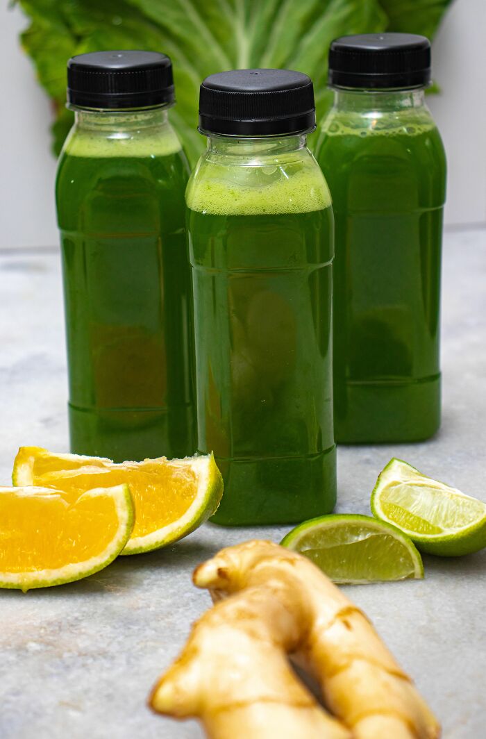 Three bottles of green juice with sliced oranges, limes, and ginger, depicting popular healthy habits.