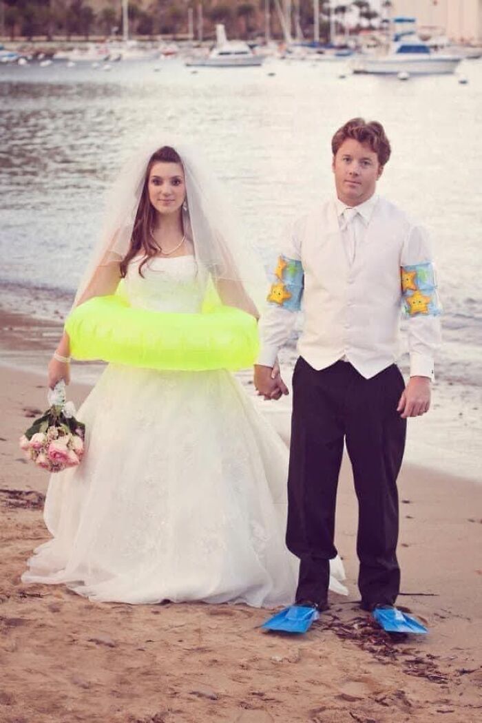 Funny wedding photo of a bride with an inflatable ring and a groom with armbands and flippers on a beach.