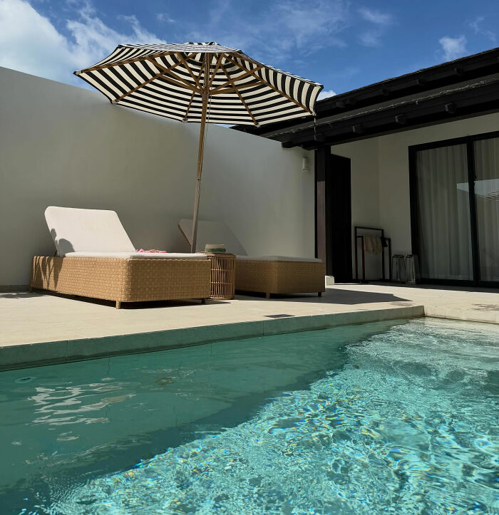 A luxurious outdoor private villa area with a swimming pool, lounge chairs, and a striped umbrella in Bali.