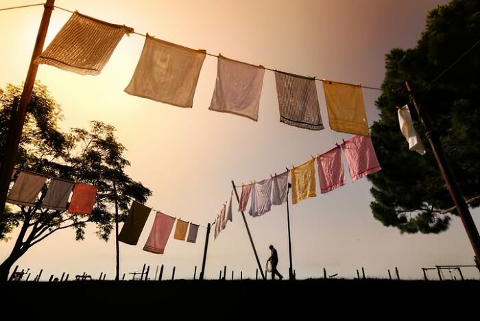 Murat Bakmaz captures the beauty of everyday life: Clothesline silhouetted against a setting sun with a person walking.