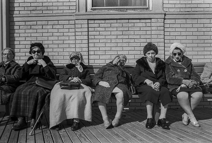 Five women sit on a bench, captured in a street photography award entry, showcasing an ordinary scene.