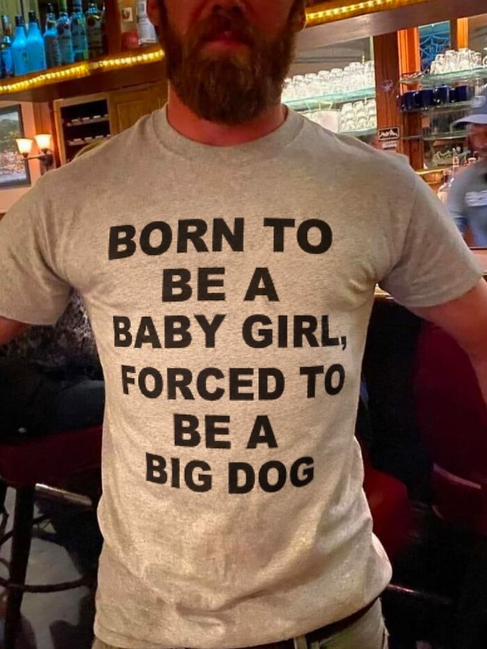 A person wearing an iconic shirt that states: BORN TO BE A BABY GIRL, FORCED TO BE A BIG DOG.