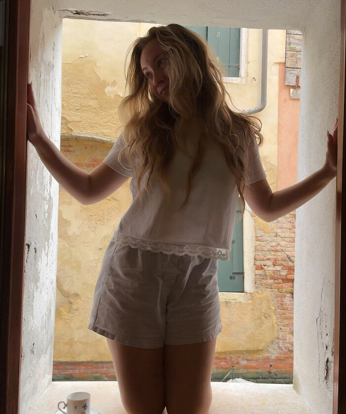 Influencer posing in a window, with a Venetian building visible outside. The influencer tries to call out Venetians. Influencer posing in a window, with a Venetian building visible outside. The influencer tries to call out Venetians.