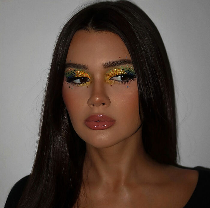 A pregnant influencer with vibrant eye makeup and long dark hair, showing off her baby bump.