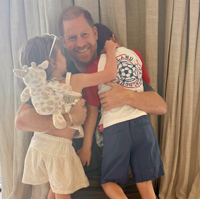 Prince Harry smiling as two children embrace him, hinting at Meghan Markle and Prince Harry's family life. Prince Harry smiling as two children embrace him, hinting at Meghan Markle and Prince Harry's family life.