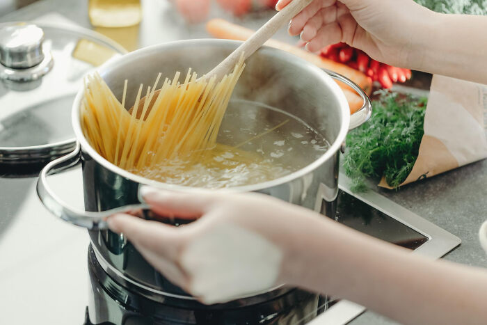 Hands stirring pasta in a pot, illustrating daily life routines that can be sources of conflict or harmony in couples and avoid divorce.