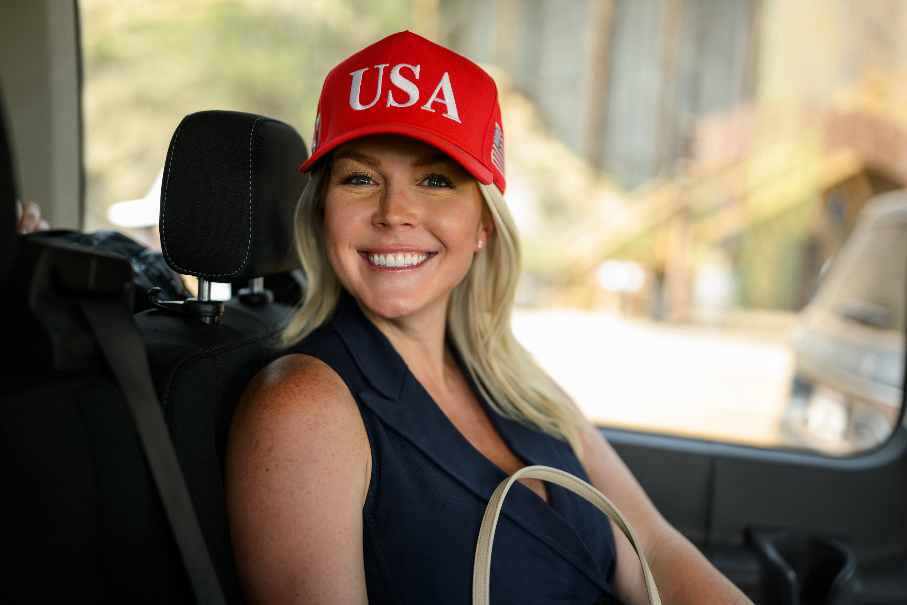 Karoline Leavitt in a red USA hat, smiling in a car, highlighting her role as press secretary.