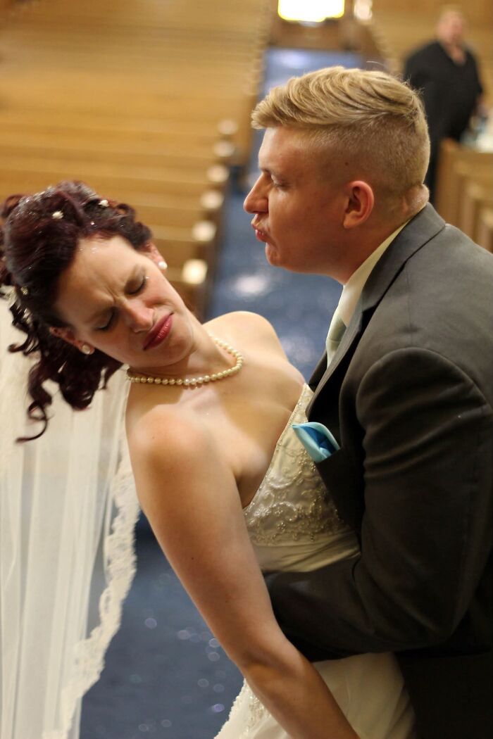 A funny wedding photo of a groom making a kissing face while holding his bride, who has a disgusted expression.