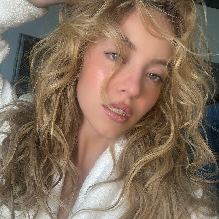 Sydney Sweeney in a bathrobe with wet, wavy blonde hair, looking directly at the camera.