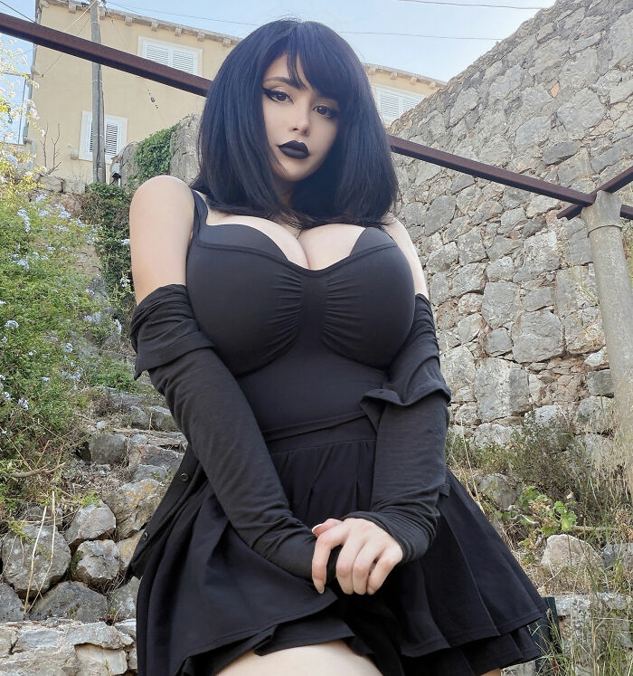 A Goth Baddie in a black dress, posing outdoors on stone steps, revealing her transformation to fans. A Goth Baddie in a black dress, posing outdoors on stone steps, revealing her transformation to fans.