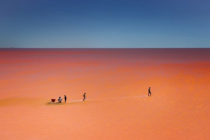 Murat Bakmaz captures the beauty of everyday life, people on an expansive, reddish-orange landscape under a blue sky.
