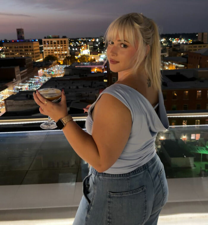 A news anchor celebrates after going viral, enjoying a drink on a rooftop with city lights in the background. A news anchor celebrates after going viral, enjoying a drink on a rooftop with city lights in the background.