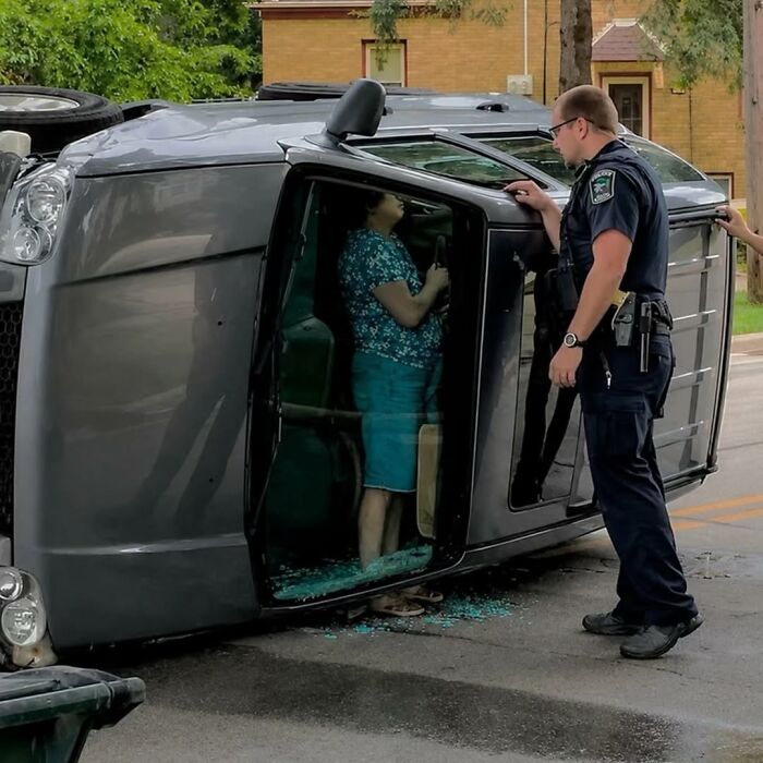 A police officer assisting a person from an overturned car, a moment captured by photographers.
