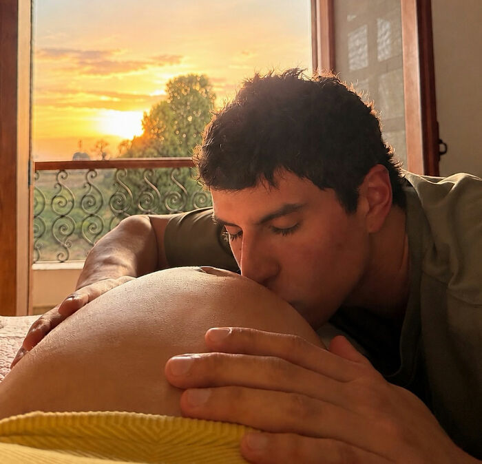 Billionaire baby's dad kissing the pregnant influencer's baby bump with a sunset visible outside the window.
