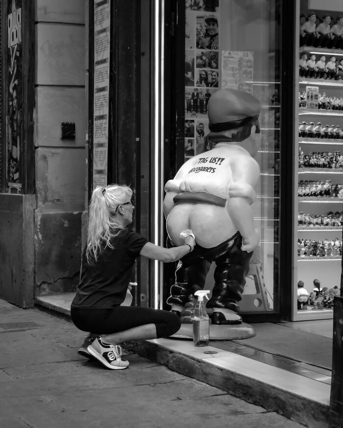 A woman cleaning a humorous large statue outside a shop, captured by photographers at a funny moment.