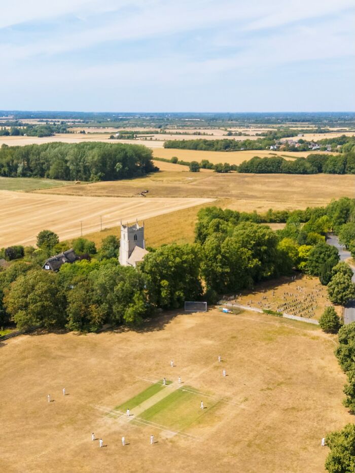 Aerial view of Europe's brutal drought showing a parched cricket field and church, highlighting the politics of drought.