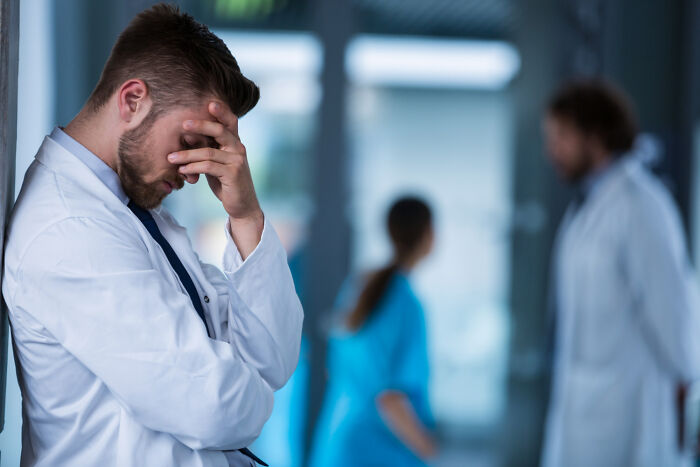 A tired male doctor leaning against a wall, appearing distressed by the hardest diagnoses he delivered.