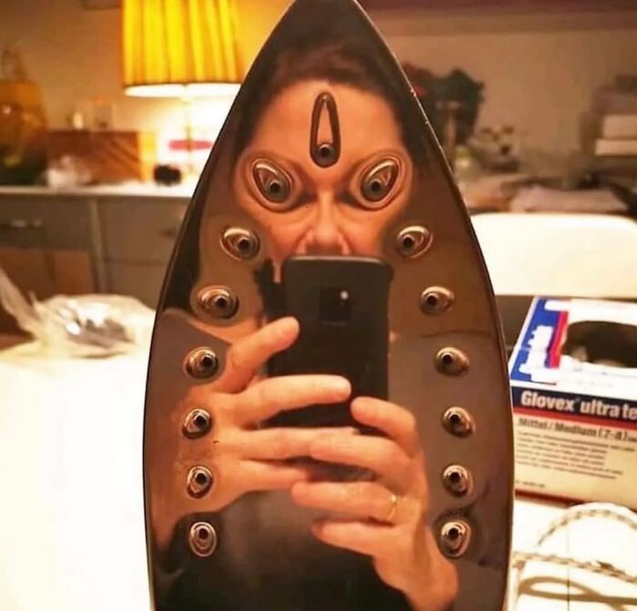 Photographers captured a woman taking a selfie in a reflected iron with multiple distorted eyes, a funny moment.