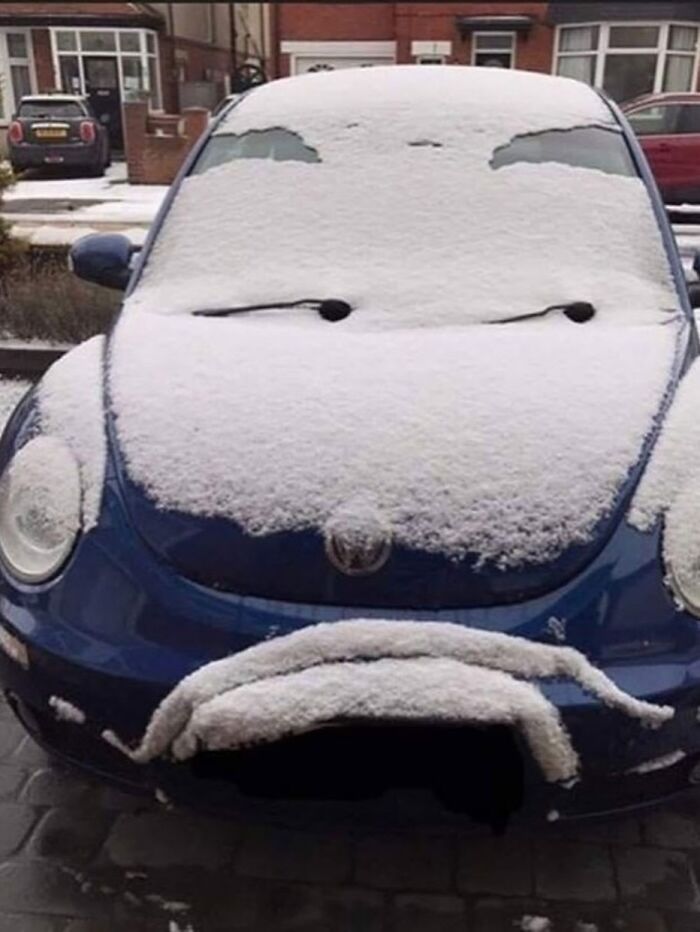 A photographer captures a blue car covered in snow, resembling a surprised or frowning face.