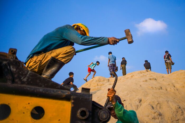 Workers on a sand pile, a Macadam Awards street photo capturing life's funniest coincidences.