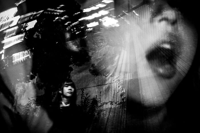 A black and white street photo with a woman's face screaming in a double exposure capturing life's funny coincidences.