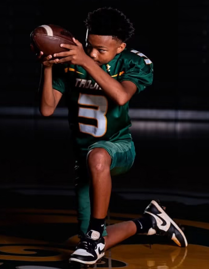 A 13-year-old football player in a green jersey kneeling, holding a football, from the viral incident. A 13-year-old football player in a green jersey kneeling, holding a football, from the viral incident.