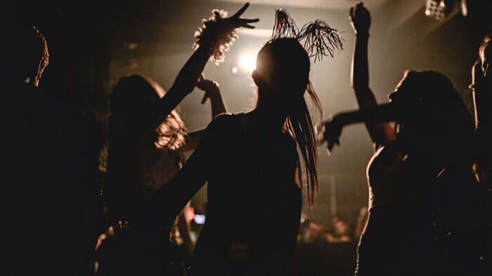 Silhouettes of people dancing in a dimly lit club with bright lights in the background, pertaining to controlling what a boyfriend eats.