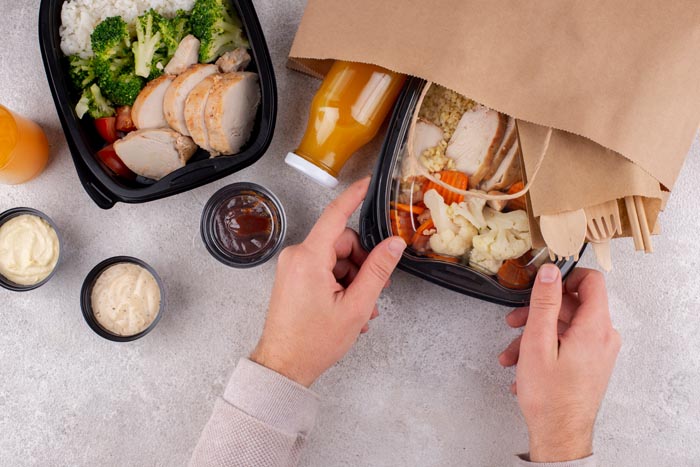 Hands arranging meal prep containers with chicken, broccoli, and juice, illustrating dumb work rules.