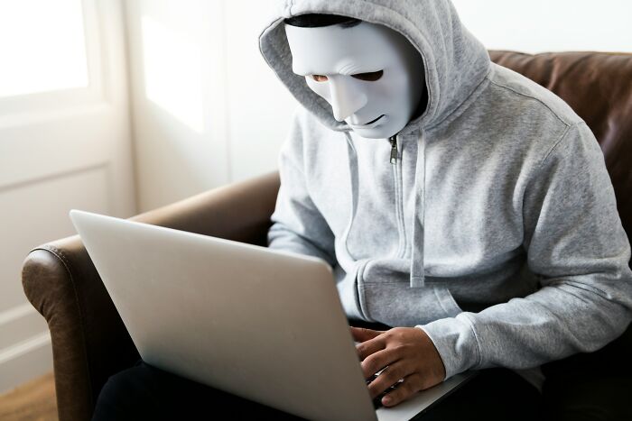 A person in a mask and hoodie using a laptop, representing widely known industry secrets and hidden information.