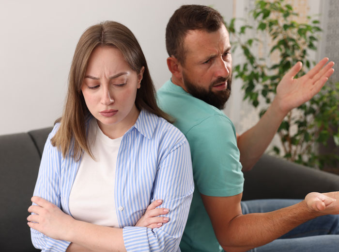 A woman looking upset, with her husband in the background looking confused, depicting marital control. A woman looking upset, with her husband in the background looking confused, depicting marital control.