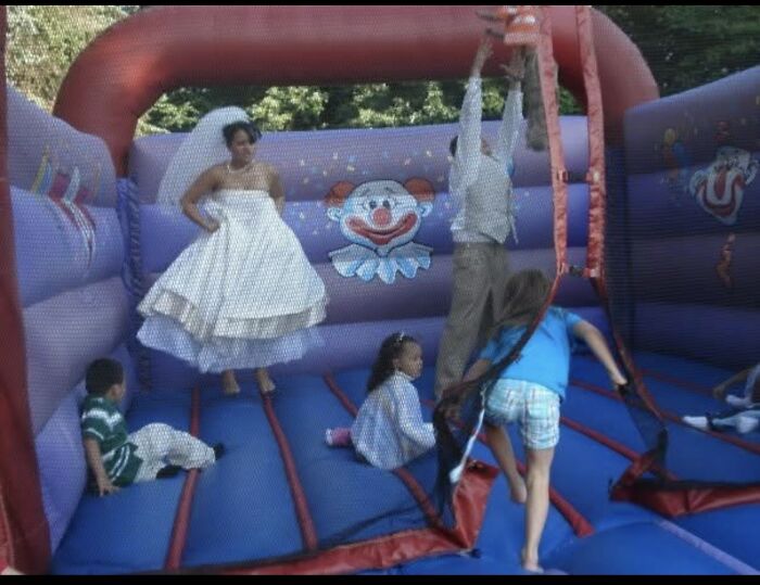 Bride on a bouncy castle, with kids and groom, enjoying funny wedding photos.