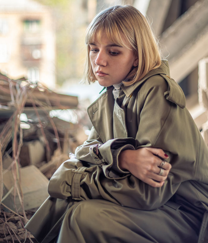 A thoughtful woman, possibly a squatter, in a trench coat, surrounded by debris, highlighting the empty property situation. A thoughtful woman, possibly a squatter, in a trench coat, surrounded by debris, highlighting the empty property situation.