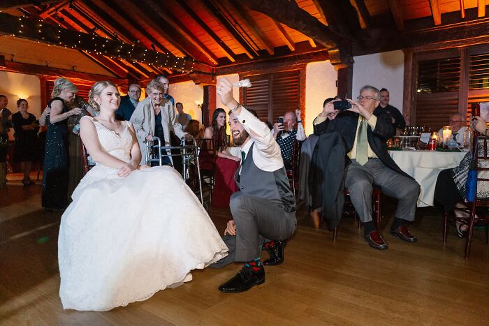 Groom takes off the garter from the bride, seated, making for funny wedding photos.