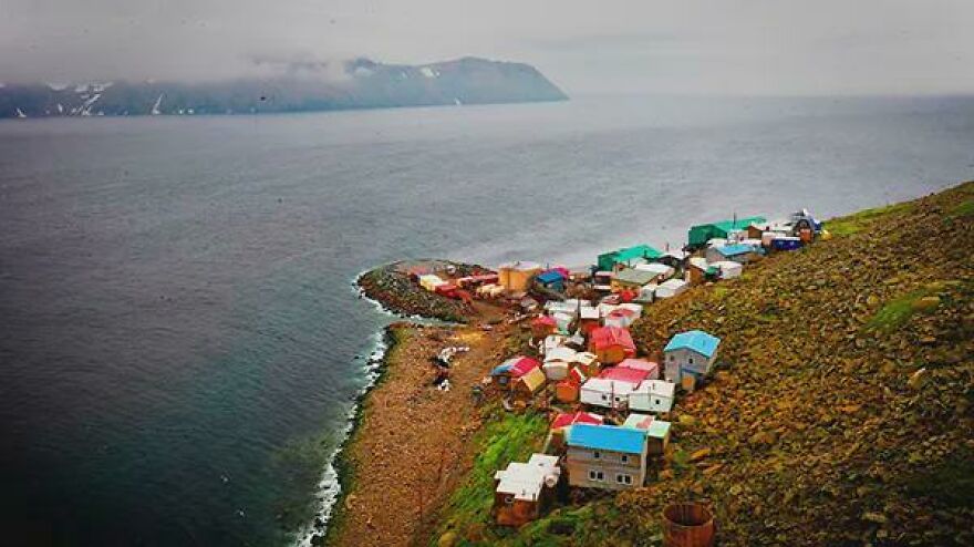 A cluster of colorful houses sit precariously on a rocky hillside overlooking the ocean, marking unusual country borders.