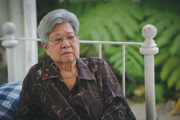 Elderly Asian woman with grey hair and glasses, looking somber, reflecting the costly price of a kidney donation. Elderly Asian woman with grey hair and glasses, looking somber, reflecting the costly price of a kidney donation.