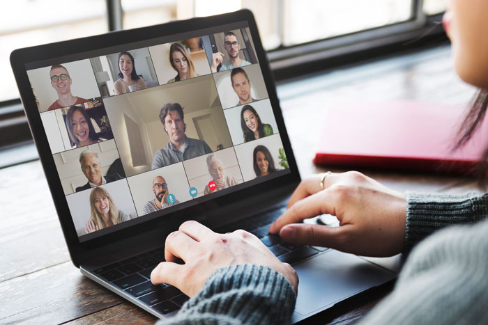A person participating in a virtual meeting on a laptop, surrounded by multiple video feeds of other participants.