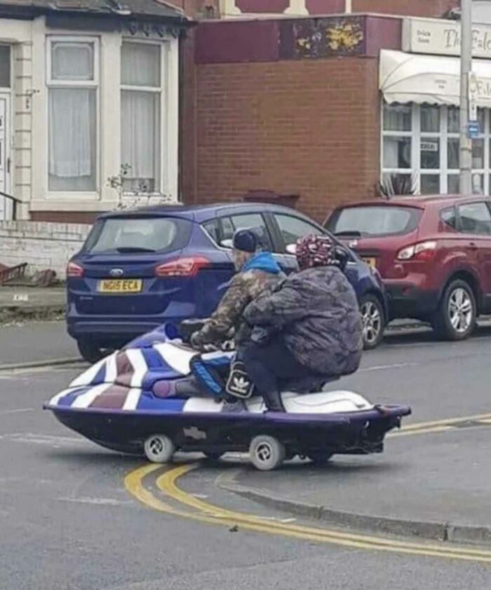 An elderly couple on a modified jet ski with small wheels, driving on a street, a scene of British humor.