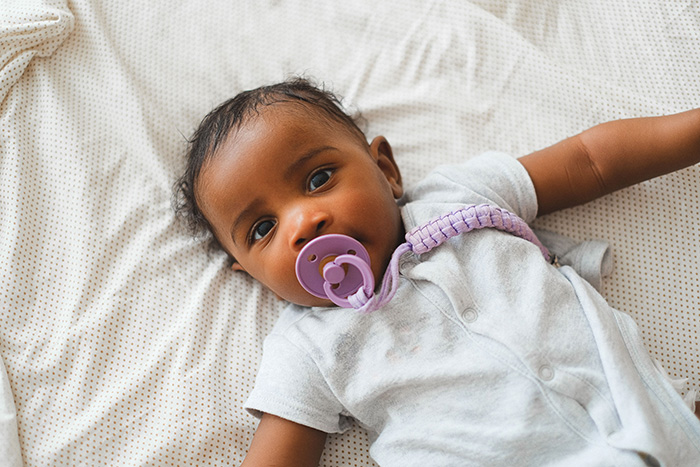 A baby with a purple pacifier, lying on a light-colored blanket, after giving birth.