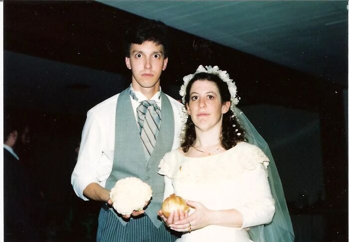 Funny wedding photo of a groom and bride with comical expressions holding an onion and cauliflower.