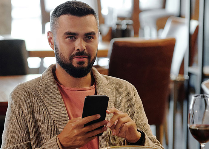 A man sitting at a restaurant checks his phone, remembering his worst first dates with women.