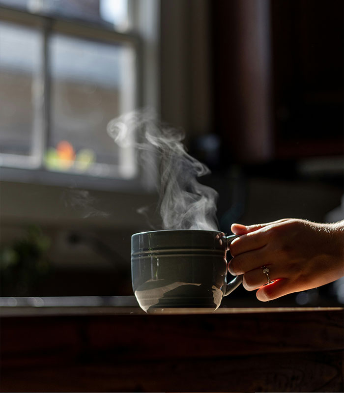 A hand holding a steaming mug, representing habits parents should never allow their children to develop.