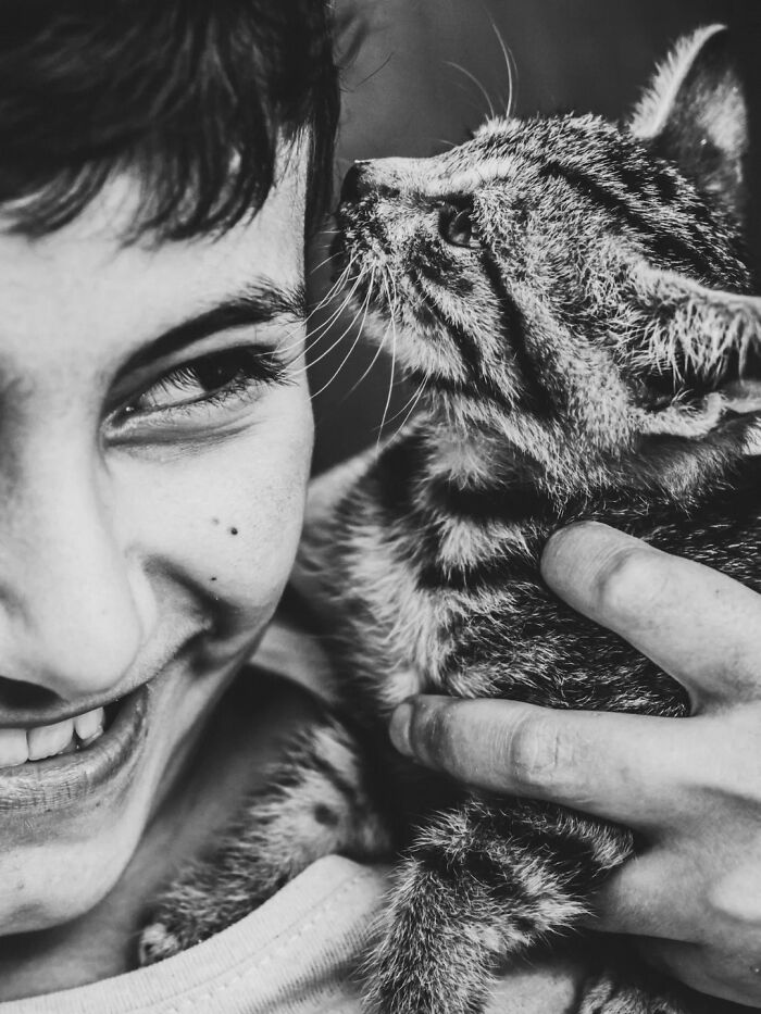 Close-up Mehmet Bayram street photo of a smiling person holding a cat close to their face.