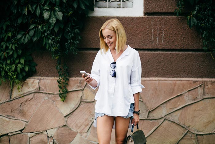 A smiling blonde woman in a white shirt looking at her phone, representing dumb work rules.