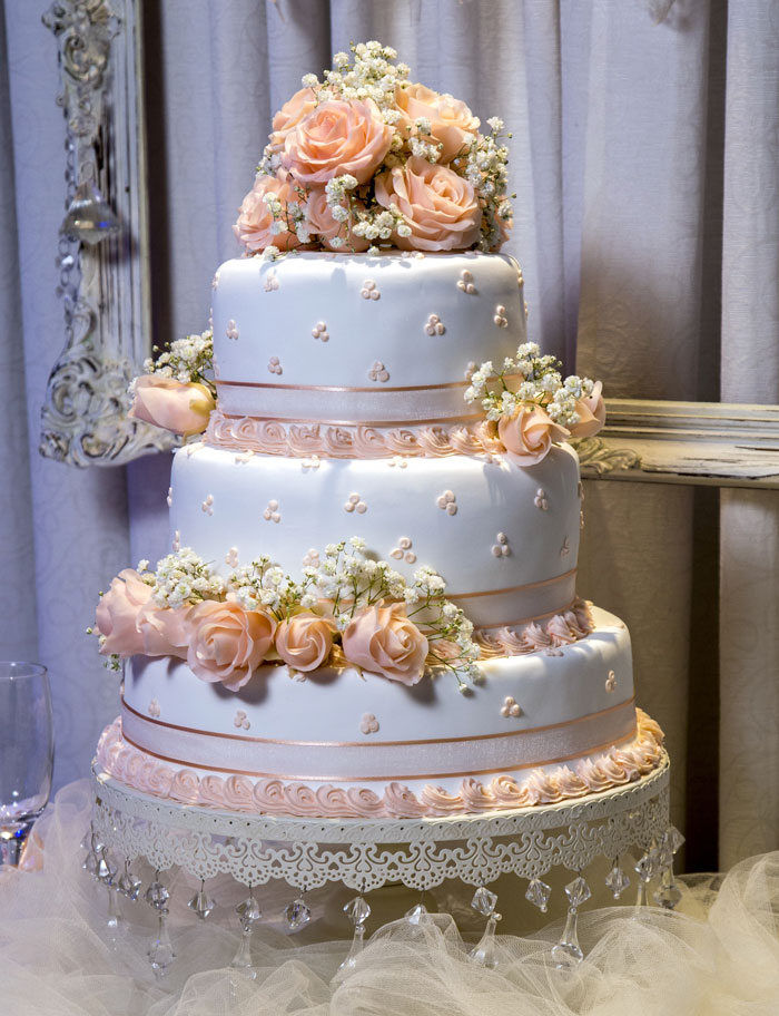 An elegant tiered wedding cake adorned with peach roses and white details, a centerpiece for any wedding.